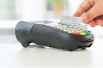 A person swipes a credit card through a payment terminal, representing a transaction or electronic payment process.