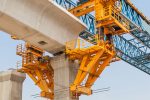 A bridge under construction with large concrete beams supported by yellow and blue steel structures against a clear sky.