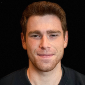 A headshot of a person with short brown hair and a slight smile against a dark background.