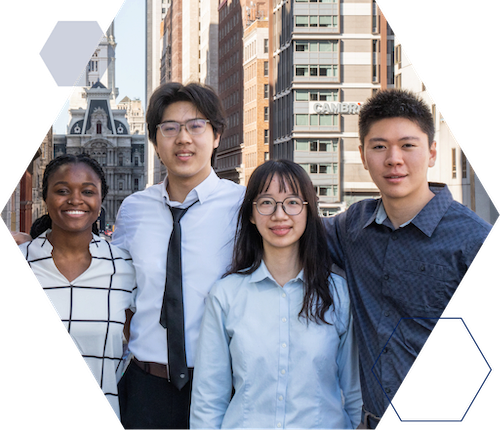 Waiai Student Research Partner Single Image A group of four people standing together outside in an urban setting with tall buildings in the background, including a historic building.