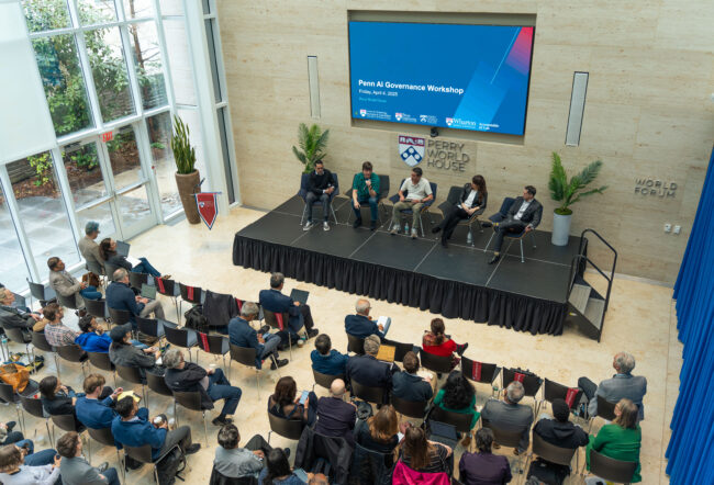 A wide shot from above shows audience members watching a panel of speakers on stage at the Wharton AI Governance Workshop