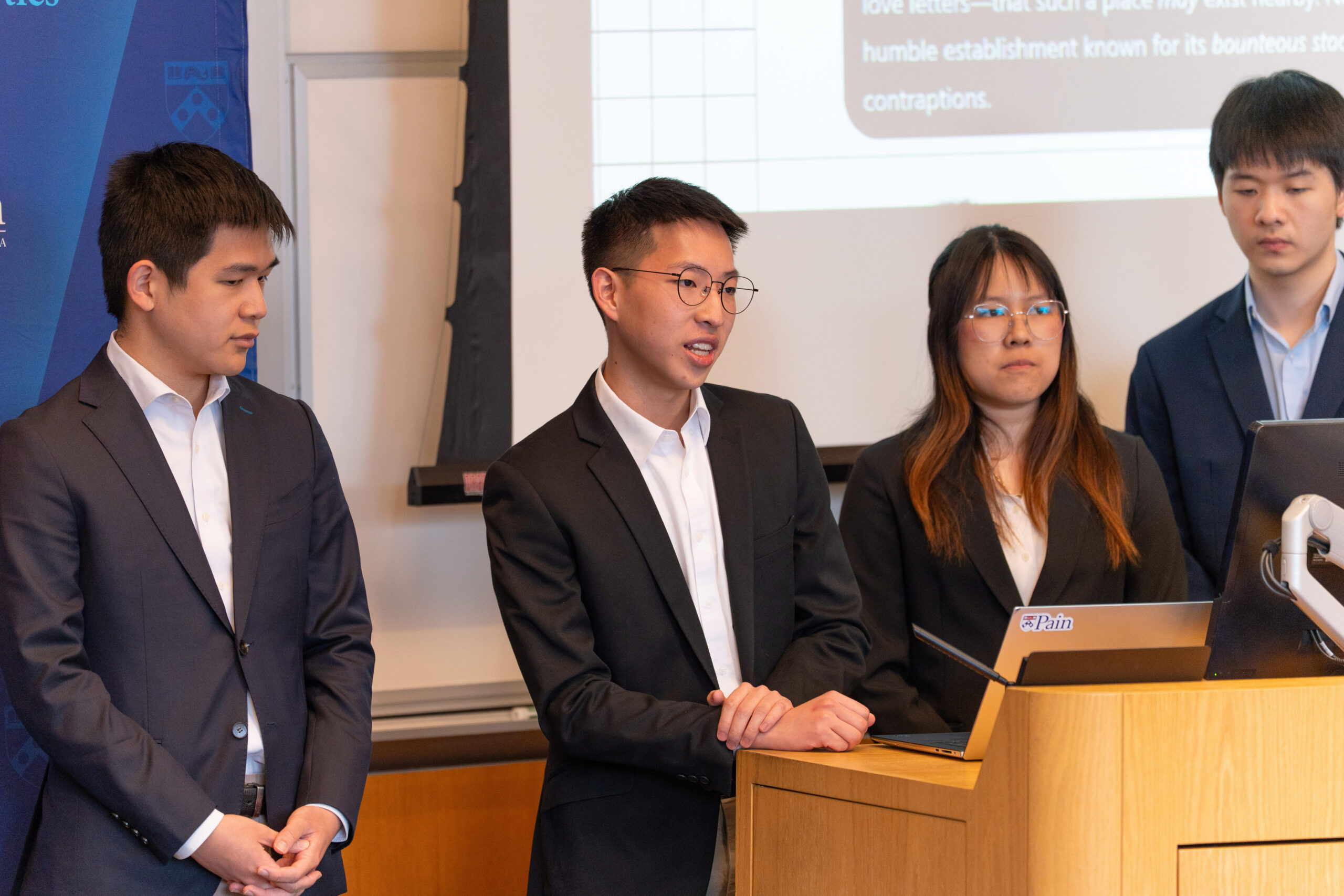 Team Haktopi Presenting A small group of people is dressed in formal attire, standing at a presentation podium with a laptop. A projected screen is visible in the background.