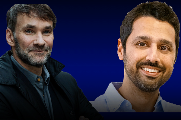 Two people smiling against a dark blue background, one wearing a black coat and the other in a white shirt.