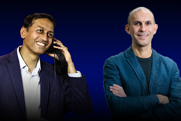 Two people smiling, one holding a cellphone to their ear. Both are wearing blazers, standing against a dark blue background.