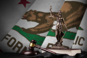 California US State Flag With Statue Of Lady Justice, Constitution And Judge Hammer On Black Drapery. Concept Of Judgement And Guilt Statue of Lady Justice alongside a gavel and books, with the California state flag in the background.
