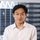 Headshot of a person in a white shirt with a blurred cityscape background.