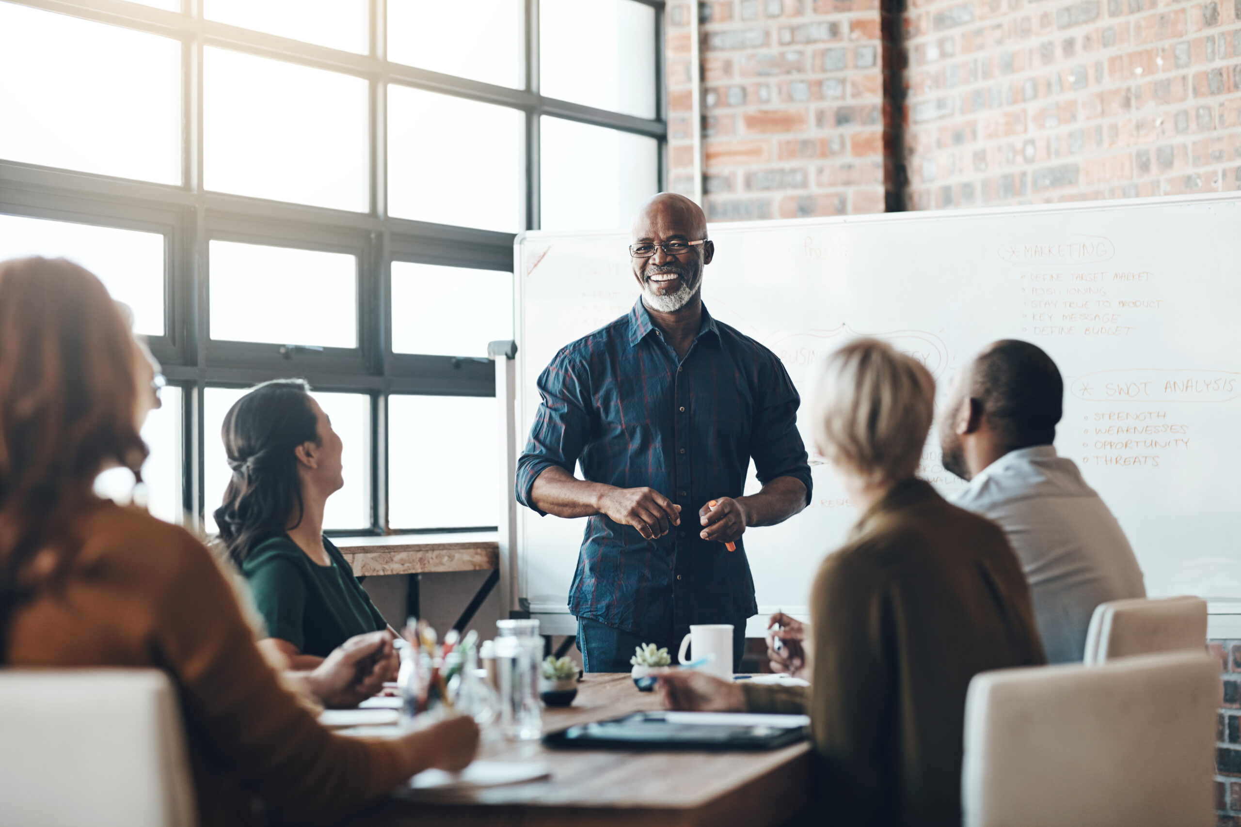 His Presentation Is Motivating. Shot Of A Businessman Giving A Presentation To His Colleagues In A Boardroom. A person presenting to colleagues in a meeting room with a whiteboard.